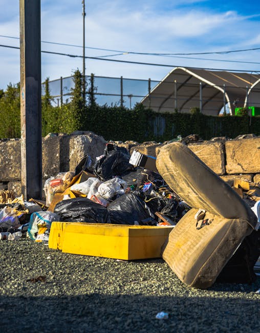 A large pile of black rubbish bags stacked against a tiled wall with visible grime and dirt, some tied tightly and others partially open, revealing occasional plastic bottles and paper waste inside. T